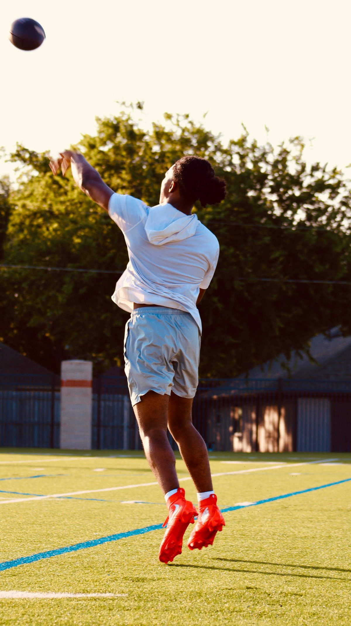 Player in light blue shirt and red socks jumping to catch a basketball on an outdoor court during daytime